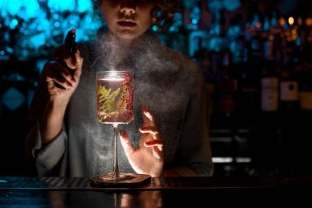 Woman bartender actively sprinkles on glass with fresh pink cocktail.の写真素材