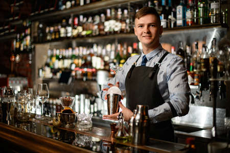Young handsome bartender holds in his hands steel shaker and empty glassの写真素材