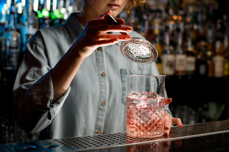 Close-up young womans hand holds strainer over large glass with pink drink