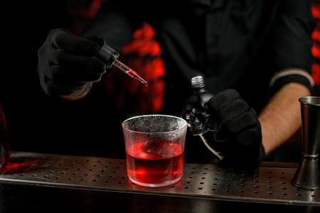 Close-up barmans hand holds dropper and adds ingredient to glass.の写真素材