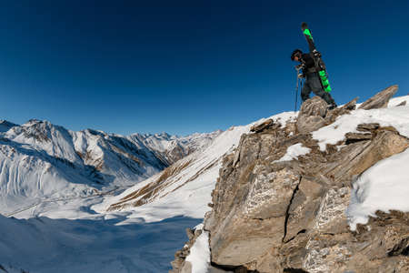 Sportsman with ski equipment on his back on rocky mountain. Beautiful mountains, blue sky and sun in background. Lack of snow in some places on the mountain is possibly caused by global warming.の写真素材
