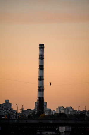 view of man balancing on stretched rope. High tower and different buildings in background