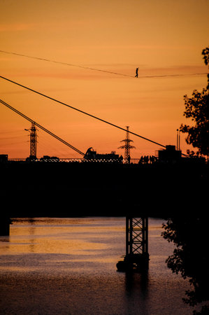 evening view of bridge over the river with stretched sling along which man walksの写真素材