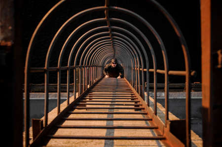 Top view man with glasses and hood climbs on high metal ladder. Sunlight falls on stairsの写真素材
