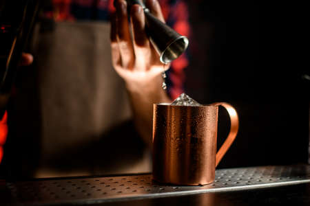 close-up metal cup over which bartenders hand hold jiggerの写真素材