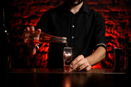 bartender in black shirt pours drink from bottle into small glassの写真素材