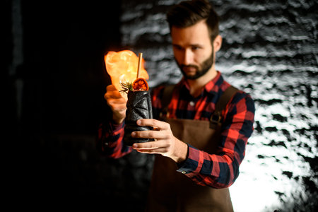 bartender holds ceramic cup with cocktail and sets it on fire.