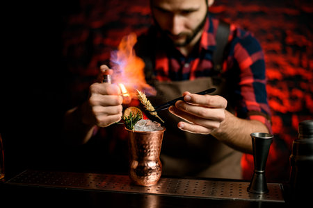 bartender holds tweezers with spikelet over metal cup and makes fire.