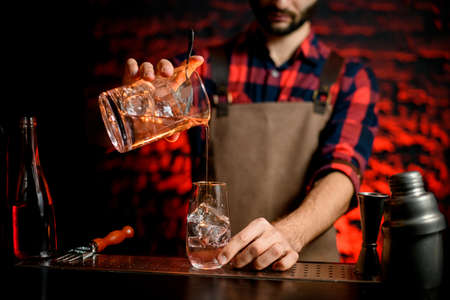 male bartender neatly pours cocktail from mixing cup into small glass.の写真素材