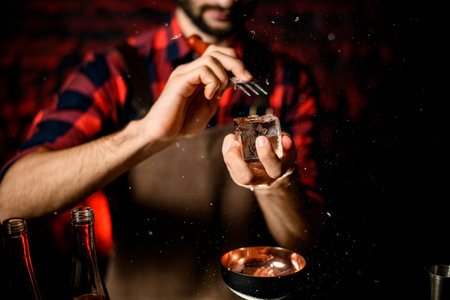 male bartender holds large piece of ice and breaks it over glass.
