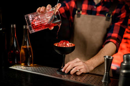 Male bartender accurate pours red campari drink from mixing cup to wineglassの写真素材