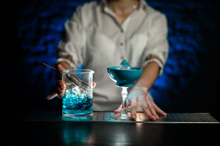 bartender's hands on blue glass on long leg and mixing cup with blue cold cocktail stand on bar...