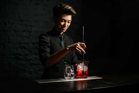 young woman bartender holds long metal spoon and mix cocktailの写真素材