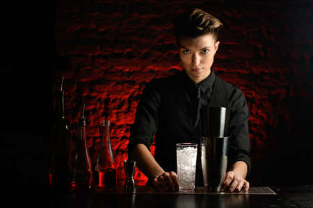 bartender stands in dark bar with different bar equipment on bar counter.の写真素材