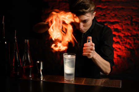 Barman makes fire over glass with cocktail on barの写真素材