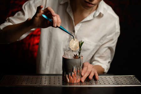 Close-up bartender accurate decorates figured glass with ice by slice of citrus using tweezersの写真素材