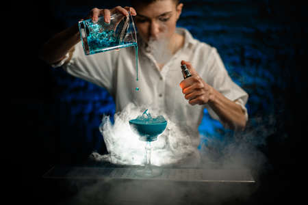 Woman bartender pours blue cocktail from mixing cup into glass at smoky bar and begin to make fire.の写真素材