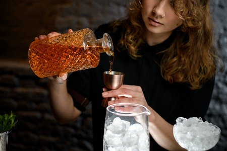 young woman bartender pours drink from bottle into jigger