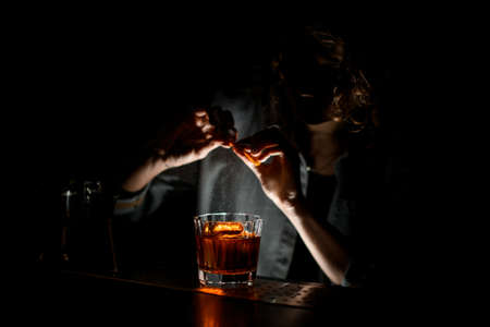 Woman bartender sprinkles to glass with cocktail on bar counter.の写真素材
