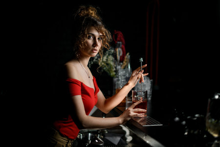 Beautiful young woman bartender mixed cocktail by long bar spoon.