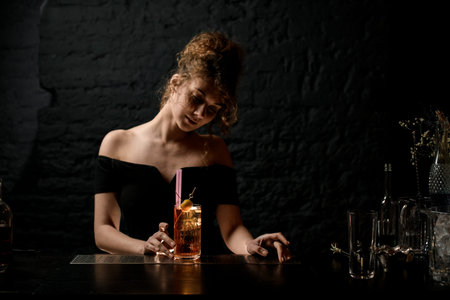 attractive young woman at bar hold glass glass with alcoholic drink decorated by berry and look at...