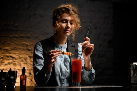 young bartender woman mixes by spoon glass with bloody mary cocktail.