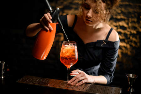 Close-up woman bartender attentively pours carbonated drink to glass with negroni cocktail.の写真素材