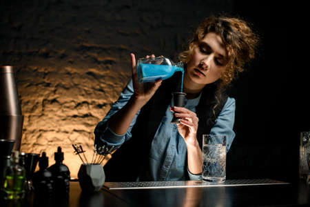 young woman bartender accurate pours drink from bottle into jiggerの写真素材