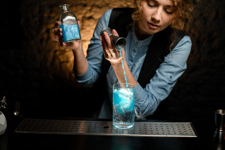 young woman at bar pours drink from jigger into glass