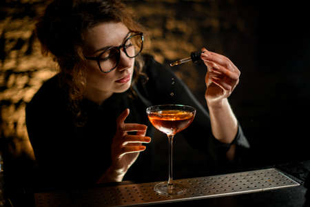 beautiful woman at bar attentively adds ingredient to glass with drinkの写真素材