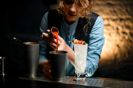 young woman barman pours bright drink from jigger into glassの写真素材