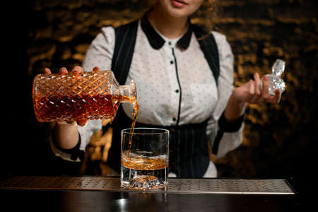 Close-up barman lady carefully pours alcoholic drink from bottle into glassの写真素材