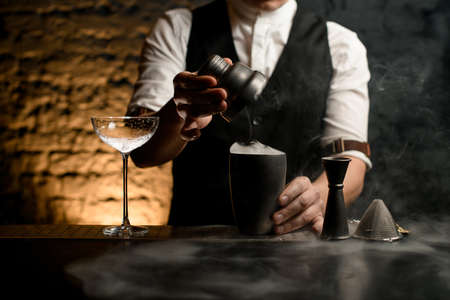 close-up male bartender holding in his hand cap from steel shaker with smoke on smoky bar.の写真素材