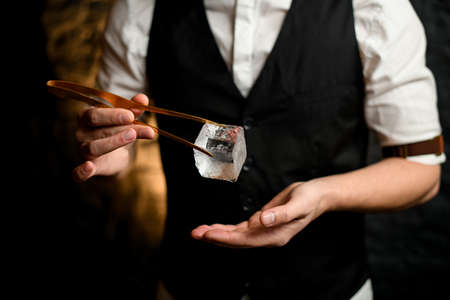 Close-up man holding big cube of ice using tweezers.の写真素材