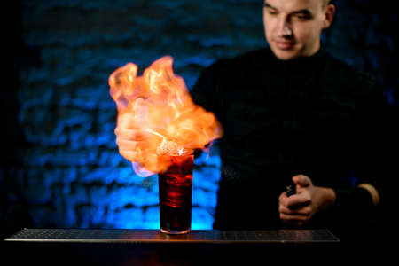 Man at bar makes fire over glass with cold alcoholic cocktail and look at itの写真素材