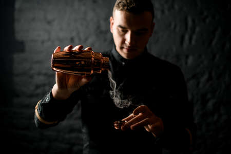 man bartender holds golden shaker from which smoke pours out.の写真素材