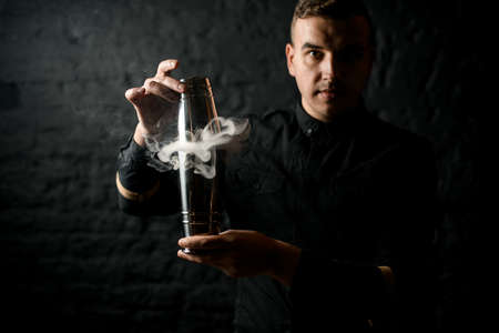 bartender in black shirt holds smoky steel shaker in his hands.の写真素材
