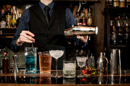 professional bartender holds steel shaker and mixes cocktailの写真素材