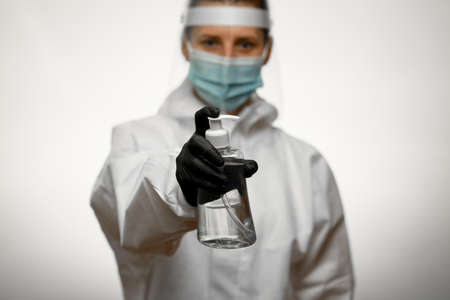 Person in full medical protective clothing holds bottle of disinfectant in outstretched handの写真素材