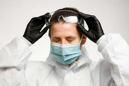 young woman nurse with closed eyes in medical mask holds hands on safety glasses to her headの写真素材