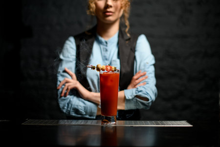 glass with Bloody Mary cocktail decorated with canapes stands at bar.