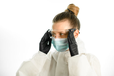 Beauty blond woman in white protective clothing puts on safety glasses on grey background.