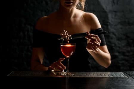 female bartender holds tweezers with white flowering branch over glassの写真素材