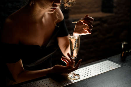 female barman holds teaspoon over glass with cocktail at barの写真素材
