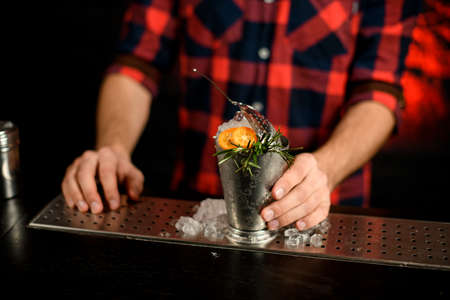 close-up of metal glass with pieces of ice decorated with green plant and yellow tomatoesの写真素材