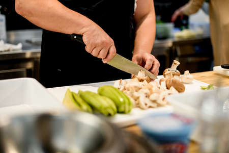 Male chef accurate cuts green zucchini and champignon mushrooms with knife into slices in order to grill them.の写真素材