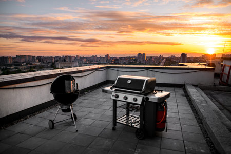 Top view of grill equipment which stands outdoor on roof of building. City and sunny sunset in...