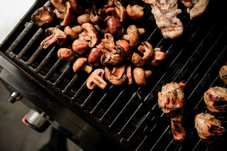 Top view on grill grid with fried mushrooms and pieces of meat.