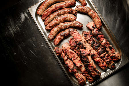 Top view of metal tray with grilled sausages and pieces of beef meat with crisp.の写真素材