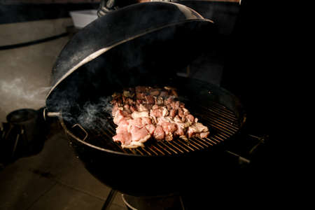 prepared pieces of raw beef meat grilled on black round barbecue. Some smoke around meatの写真素材